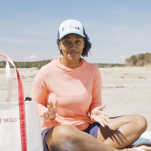 Stephanie sitting on a blanket on the beach wearing a ball cap.