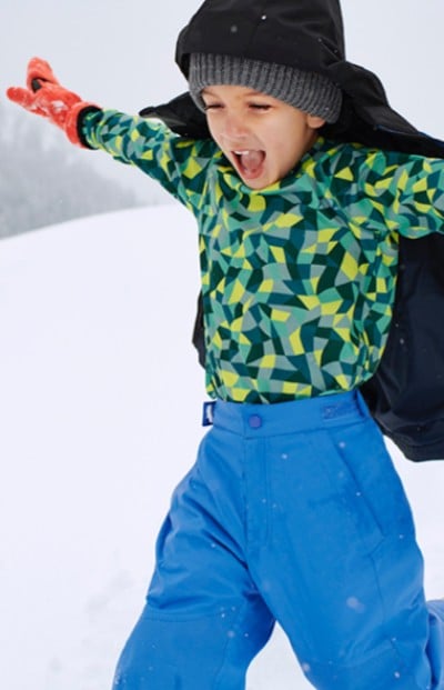 A boy in colorful L L Bean winter gear stands against a snowy backdrop, ready for some fun in the snow. 