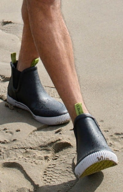 Image depicting a man wearing rain boots on the beach.