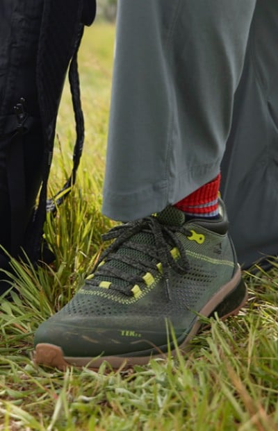 A close up of a gray shoe with yellow laces on grass, hinting at outdoor activity and adventure. 