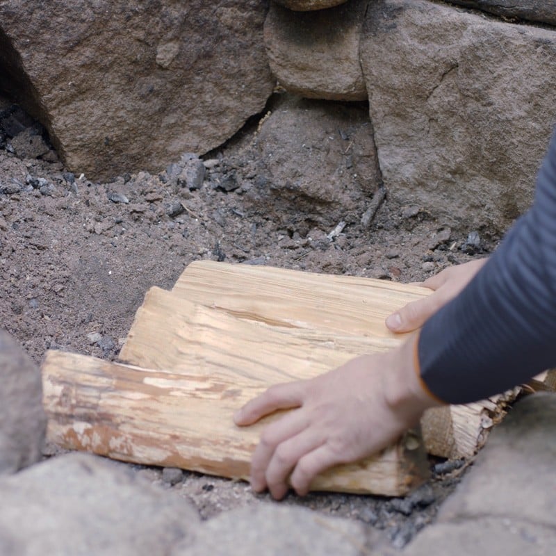 Nate arranging 4 fuel logs together in the middle of a fire ring.