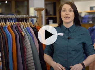 Retail Representative Nicole stands in the flagship store with a rack of outerwear, a play video button in the center.