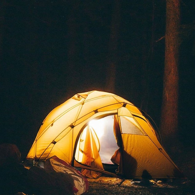 A dome-style tent at night glowing with interior light.