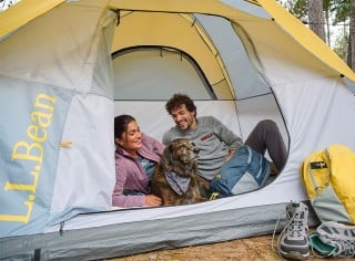 A couple and their dog sitting in a tent.