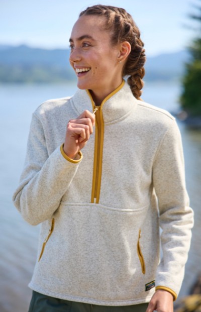 A woman in a quarter zip sweatshirt stands by a body of water. The scene is calm and outdoors. 