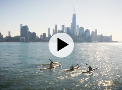 City skyline with four men kayaking in the foreground.