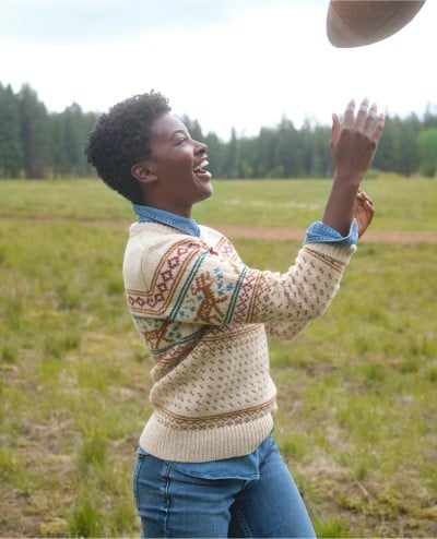 Woman outside catching a football wearing a Ragg Wool Sweater.