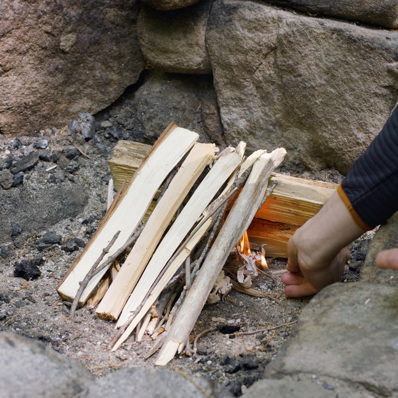 Nate adding tinder to the first layer of logs, filling the gaps between logs.