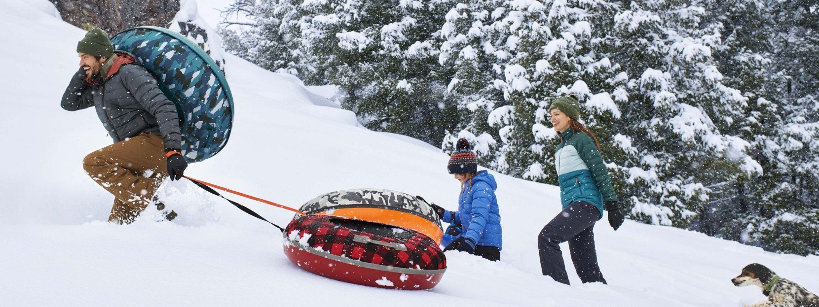 A family walking up a snowy winter hill with snow tubes.