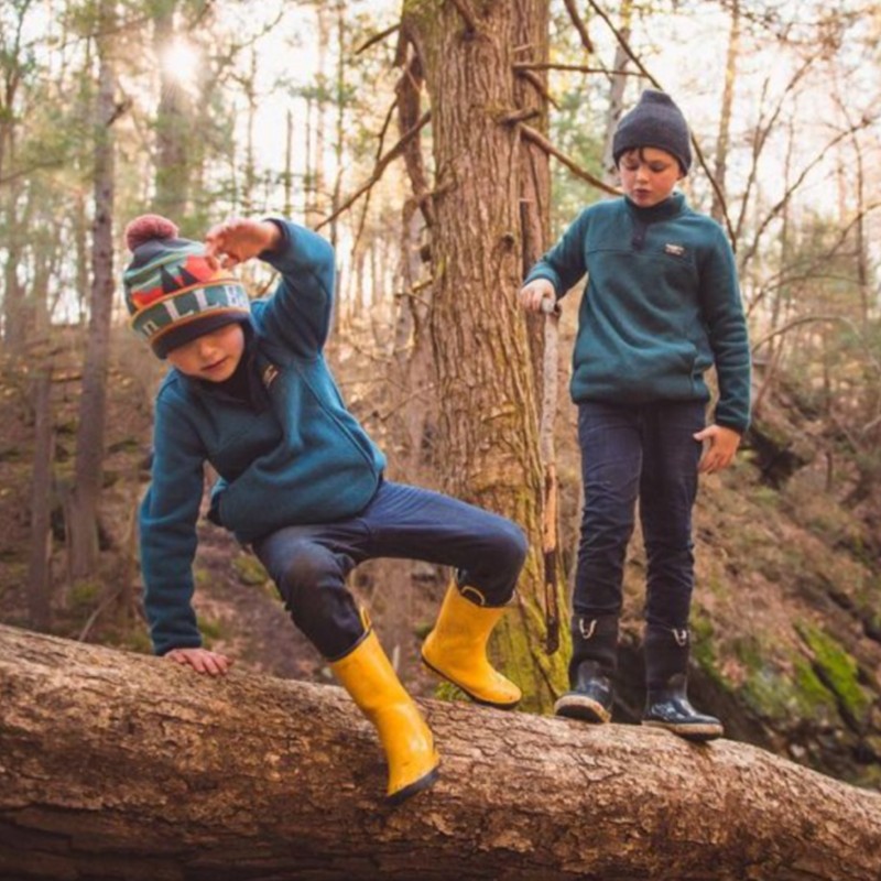 Two kids playing on a log in the forest.