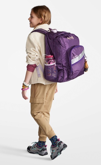 A girl from slightly behind, wearing a purple deluxe school backpack.