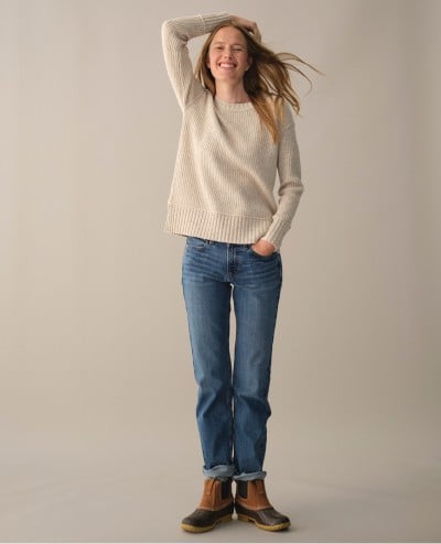 A woman standing with heels together, one forearm on her head the other had in her jeans pocket, wearing a Women's Heritage Heirloom Sweater.