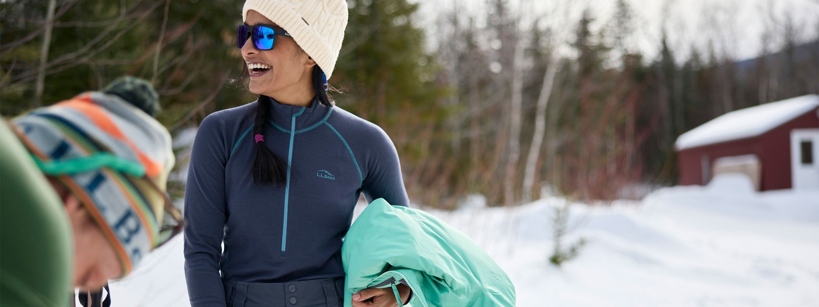 Smiling woman outside in winter, wearing a baselayer top and holding a jacket.