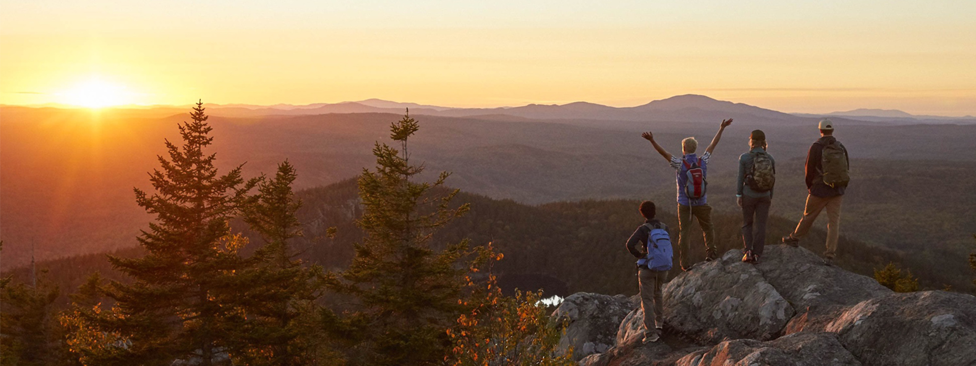 4 hikers standing on the top of a mountain watching a sunrise.