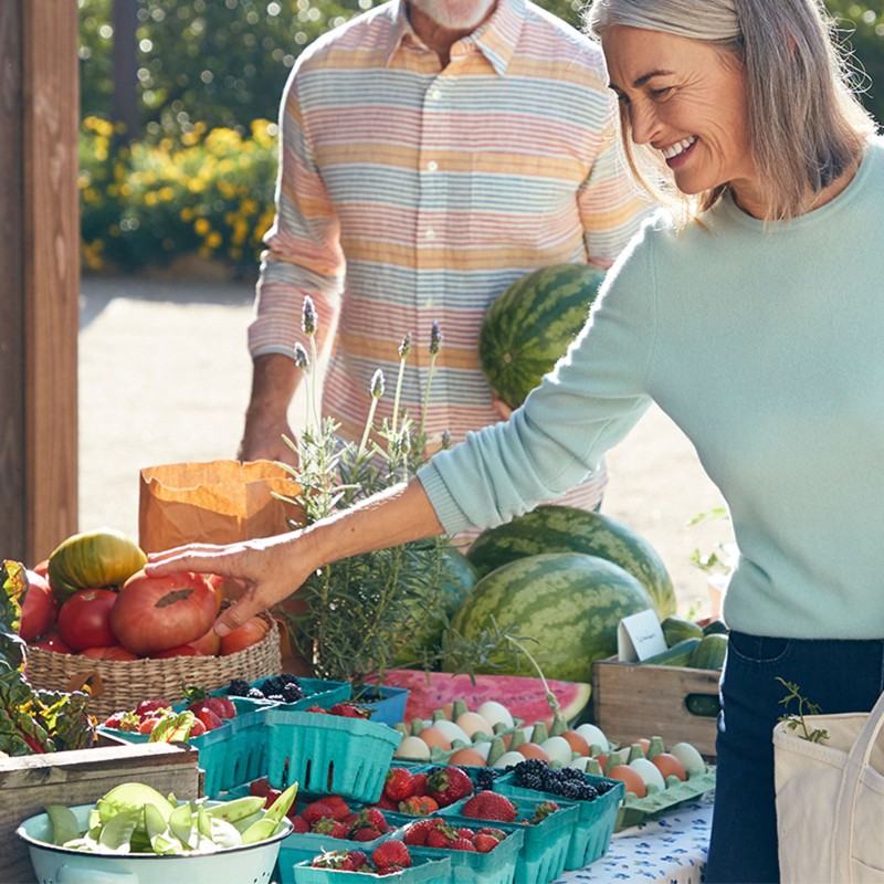 Smiling woman picking out vegetables at a farmer's market.