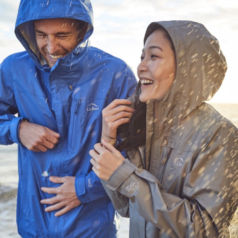 A man and a woman wearing rain jackets with hoods up, walk arm-in-arm in the rain.