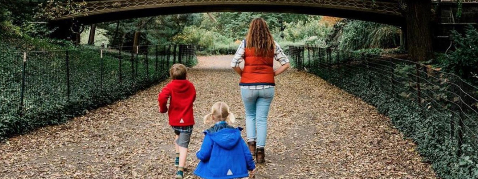 A mom and two kids walking on a leaf covered walkway.