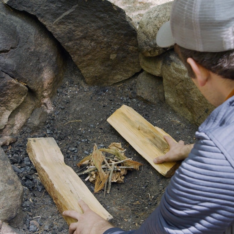 Nate placing a fuel log on either side of a pile of tinder.