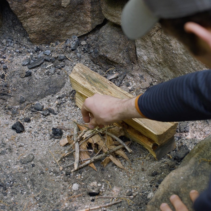 Nate adding tinder to the first layer of logs, filling the gaps between logs.