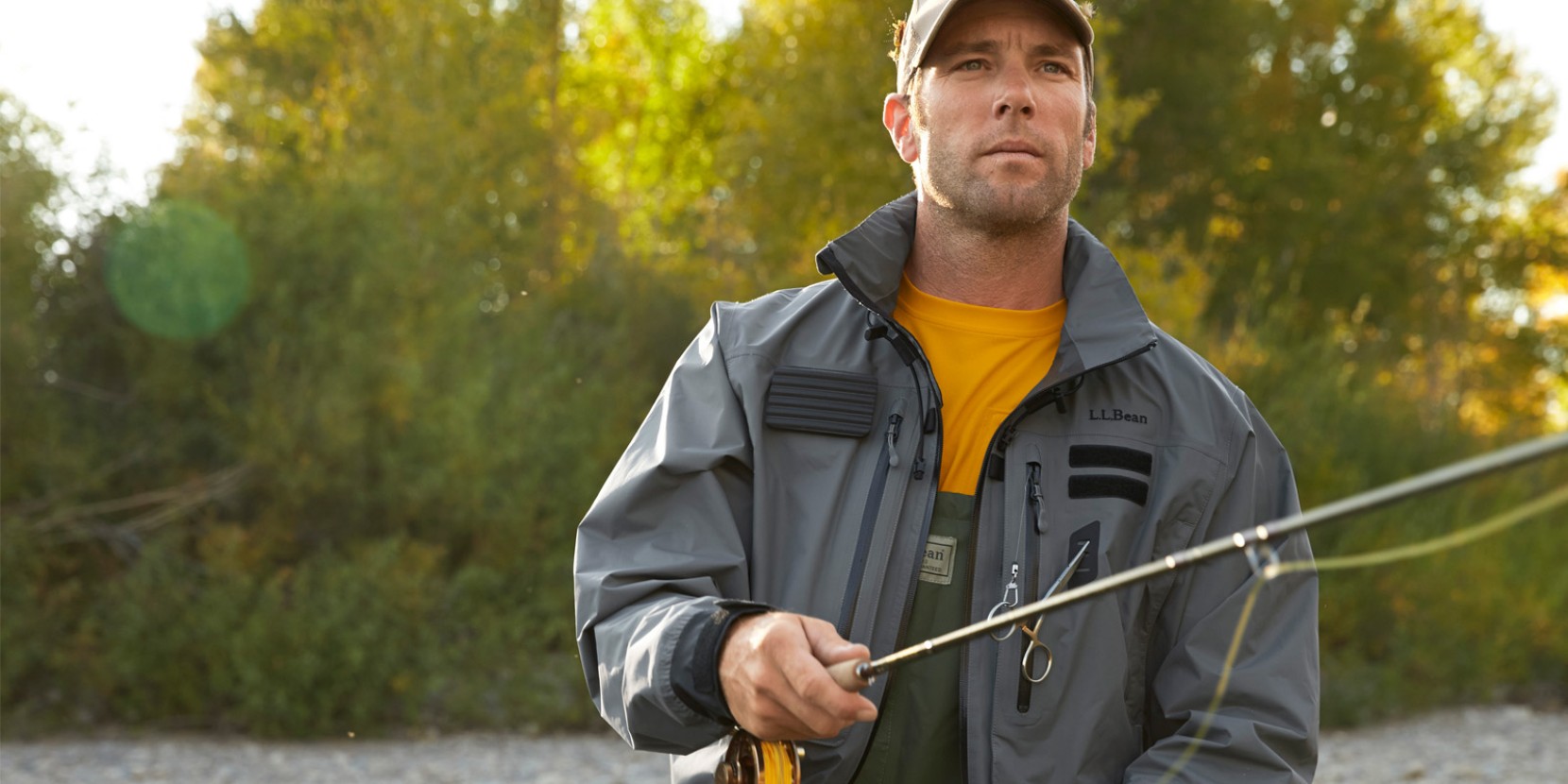 A man fly-fishing in a river wearing a fishing rain shell.