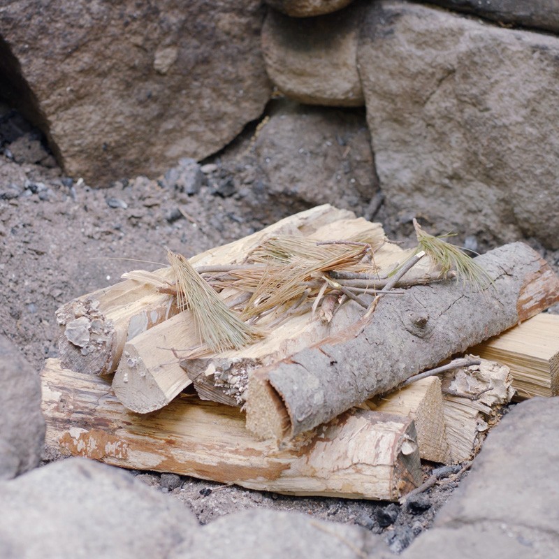 Nate adding tinder to the first layer of logs, filling the gaps between logs.