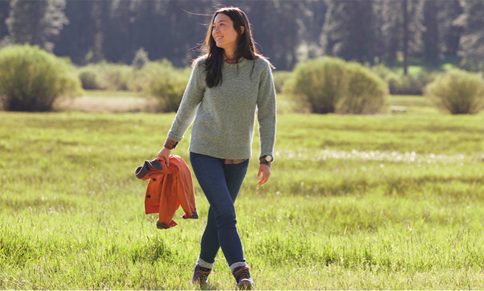 A woman walking across a field wearing a ragg wool sweater.