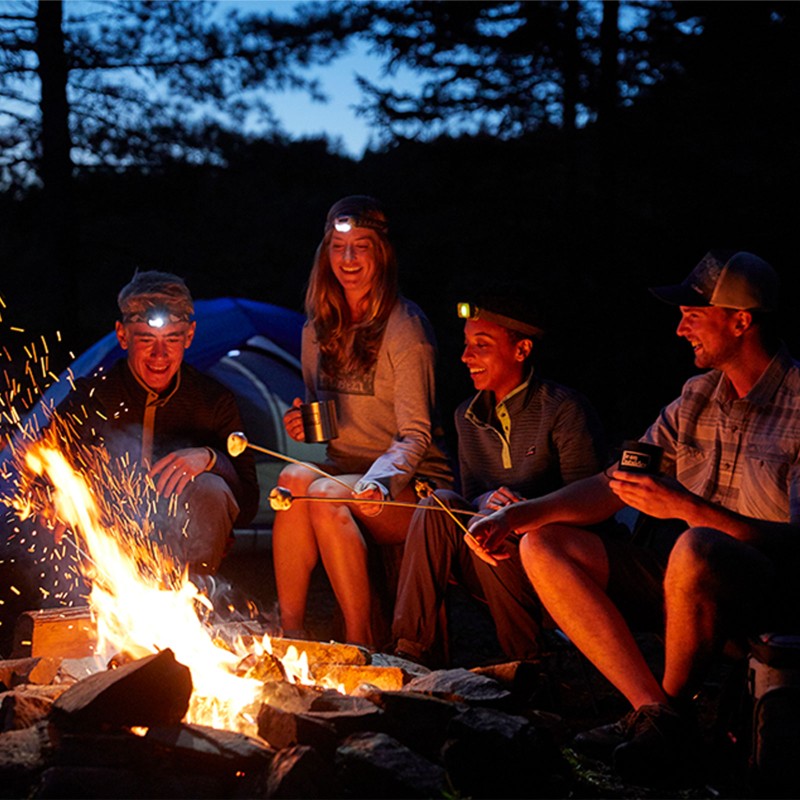 Friends wearing headlamps toasting marshmallows around a campfire.