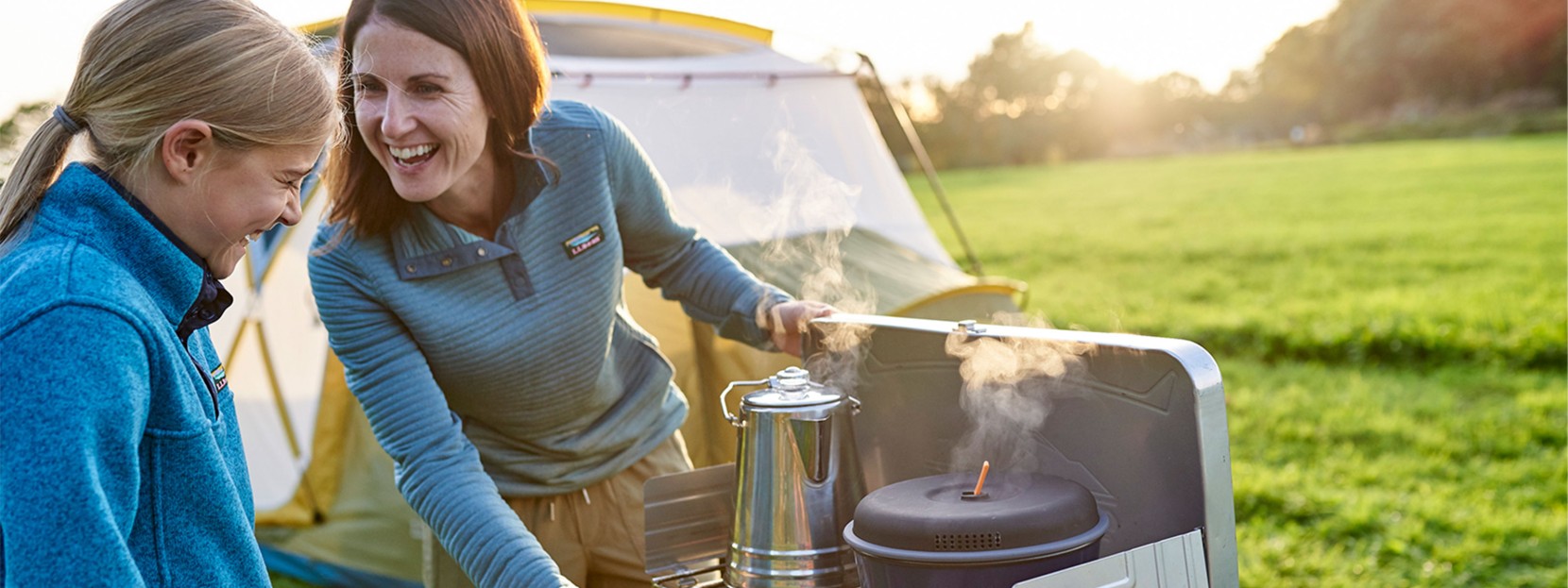 Mother and daughter cooking and laughing at their campsite.