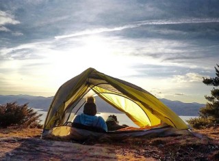 A person and a dog inside a tent watching the sunset.