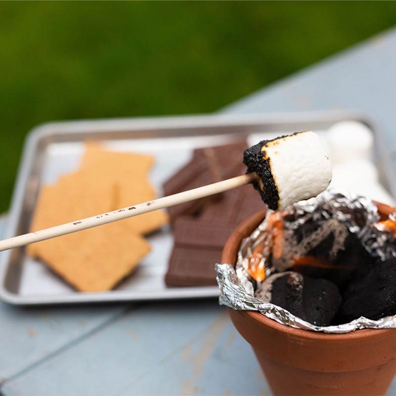 A close-up of a small terra cotta pot with foil cooking a marshmallow.