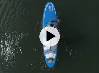 A kayak instructor outside with several kayaks, play video symbol in the center.