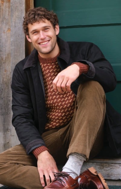 An man sits on steps, wearing a casual jacket and a patterned sweater.