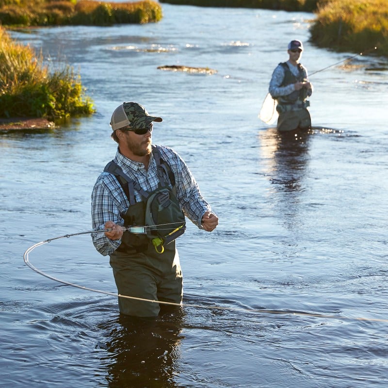 Two men standing in water and fishing.